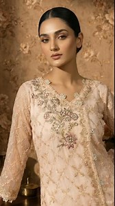 This breathtaking ensemble is a pastel pink angharka-style embroidered outfit, blending traditional South Asian elegance with a touch of modern refinement. Crafted in a soothing blush-peach hue, the outfit features a beautifully tailored angharka silhouette, distinguished by its overlapping front panels and intricate detailing. The fabric is delicately adorned with thread embroidery in geometric pattern, forming a soft lattice design enhanced with subtle hints of sequins that add a graceful shim