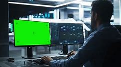 Professional Male IT Technical Support Specialist and Software Developer Working on Computer with Green Screen Mock-display in Monitoring Control Room. Programmer Fixing Hiccups in Service