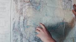 A man searching for a location on a wall map. His finger points to a position on the large map