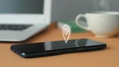 Animation of GPS geolocation icon on smartphone display against laptop and coffee cup background in office.