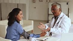 Mature Indian doctor man measuring blood pressure of positive Hispanic patient woman, using measurement electronic tool for cardiac diagnosis, medical examination, finding perfect checkup result
