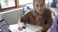 Two happy asian muslim women wearing hijab working together with using laptop pc tablet and talk about success working in an e-commerce business.