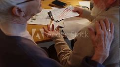 Medium rear shot of elderly Caucasian husband and wife opening letter from utility provider or mortgage bank, taking out unpaid bill or missed payment notice, consoling each other and holding hands