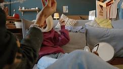 Stab shot of Caucasian teenage girl with cerebral palsy wearing blond wig and pink y2k glasses sitting on floor in modern living room dancing and chatting with friend, chilling together indoors