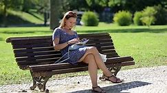 young girl sitting at the bench in a park and making notes