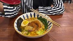 a woman who is enjoying tom yum ramen noodles with toping ebifurai, egg, corn, nori, bokchoy, leek in restaurant Japanese
