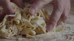 Close up video of hands shaking tagliatelle pasta. Slow motion of home made pasta on table.
