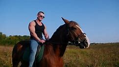 Strong man bodybuilder in a black t-shirt, denim pants, sunglasses riding a horse