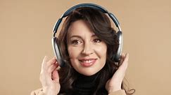 Mature woman listening streaming music, enjoying dance with headphones on beige