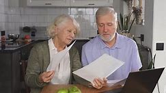 An elderly husband and wife pay the bills and manage the budget. A retired couple checks their accounts using a laptop while sitting at a desk at home.