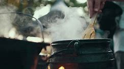 rustic pot on fire cooking hot food steaming slow motion stirring wooden spoon