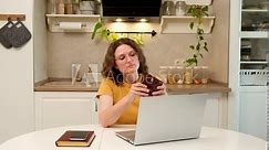 A woman with a laptop holds an empty wallet without money while sitting at a table in a home kitchen. An adult female businesswoman works from home, a remote office
