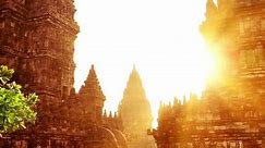 Beautiful buildings of ancient Prambanan or Rara Jonggrang Hindu temple complex against shining morning sun on background. Java, Indonesia. Amazing touristic landmark at sunrise. Camera zooms out.