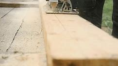 Male carpenter using electric circular saw in backyard workshop with wood chips flying. Building contractor worker cutting plank by fretsaw tool to cut boards on new home construction project. Sawing