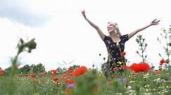 Blonde woman listen a music in headphones in poppy flowers fields in summer