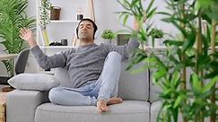 Latin young man listening relaxing music on sofa.