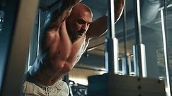A muscular bodybuilder with a bare torso engages in a rigorous workout using a cable crossover machine in a modern gym setting, highlighting his well-defined muscles and strong physique. Camera 8K RAW
