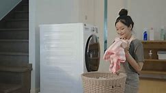Happy young asian woman opening and removing clean laundry from the washing machine and putting the clothes in a basket, Tired housewife working, smell