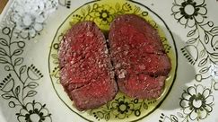 Top view of ribeye strip steaks roasted with spices and seasoned with olive oil on designer floral dish. Freshly cooked to perfection beef cut in two halves and showing succulent tender red meat.