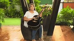 Happy mature middle aged woman sitting on chair singing play acoustic guitar enjoy music spend free time outdoor home. Beautiful smiling Indian female guitarist practice tuning on musical instrument