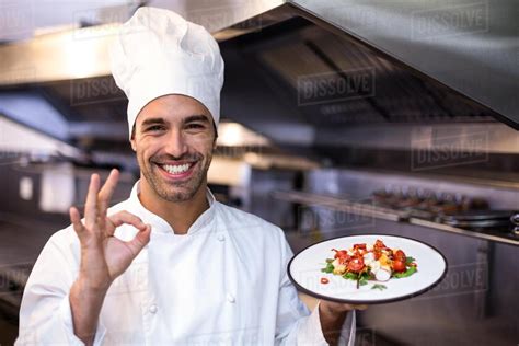 Los diseños más comunes están disponibles en nuestras instalaciones para consumo inmediato. Handsome chef showing ok sign and meal in a commercial ...