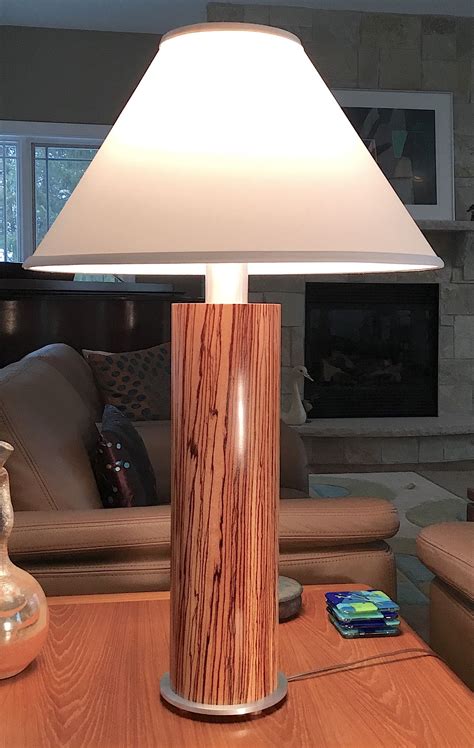 The top is made of solid reclaimed wood, providing each table its own individual character and plenty of surface area for your books, tablets, decorative arrangements, and more. TABLE LAMP-Zebra wood veneer with aluminum components ...