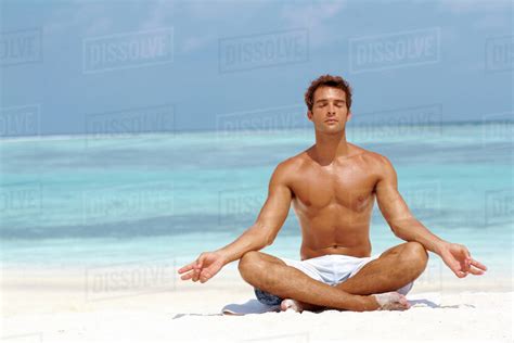 Handsome young man meditating in a lotus position on the beach - Stock ...