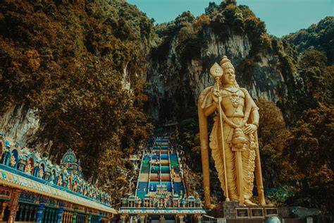 A massive flight of stairs next to giant golden hindu god leading up to what is known as temple cave. Discovering the Amazing Batu Caves of Malaysia - Dramaz