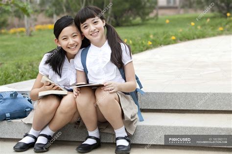 Schoolgirls sitting on steps with books and smiling ...