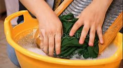 Woman diligently washes clothes by hand using washboard. Laundress skillfully uses old washboard and basin for washing dirty clothes