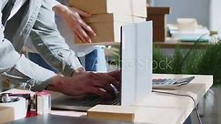 Close up shot of a man hands working on a laptop while conducting inventory and managing parcels, packages in a warehouse, storage or postal office. He working with his woman colleague.