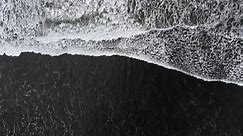 Premium stock video - Top down drone shot, waves rush up black sand beach shore