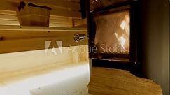 Woman adding block of wood to fire stove in traditional wooden Finnish sauna