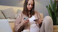 Pregnant woman shopping online using smartphone and credit card at home expectant mother purchasing from internet while sitting on floor near couch in living room