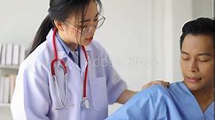 Female doctor doing physiotherapy and diagnosing male patient arm and shoulder pain in hospital examination room.