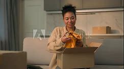 African American ethnic woman happy girl homeowner renter unpacking box on sofa moving in new home cheerful smiling female customer unpack parcel order clothes online shopping delivery relocation day