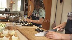 nine-year-old twins cutting sushi rolls with knives, wearing aprons and chef's hats, concentrating on rolling nori seaweed with rice, tofu and avocado.