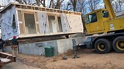 Ranch style modular home being set on foundation by crane.