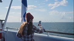 Woman sailing on cruise trip liner, girl standing on ship, taking pictures for social media, traveling on ferry, brunette in shirt and hat admiring ocean. Enjoying traveling and adventure. Finland